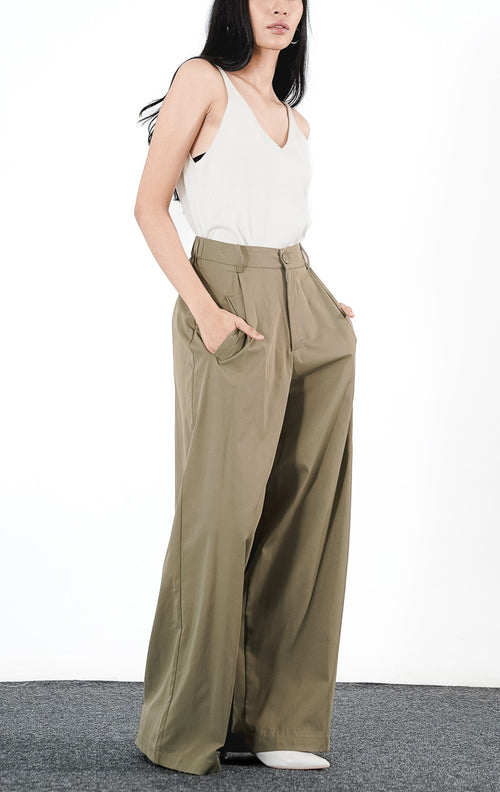 Model mengenakan Nathaniel Pants warna olive, celana panjang bahan dengan potongan lurus (straight leg), saku samping, dan ban pinggang minimalis dengan kancing senada.