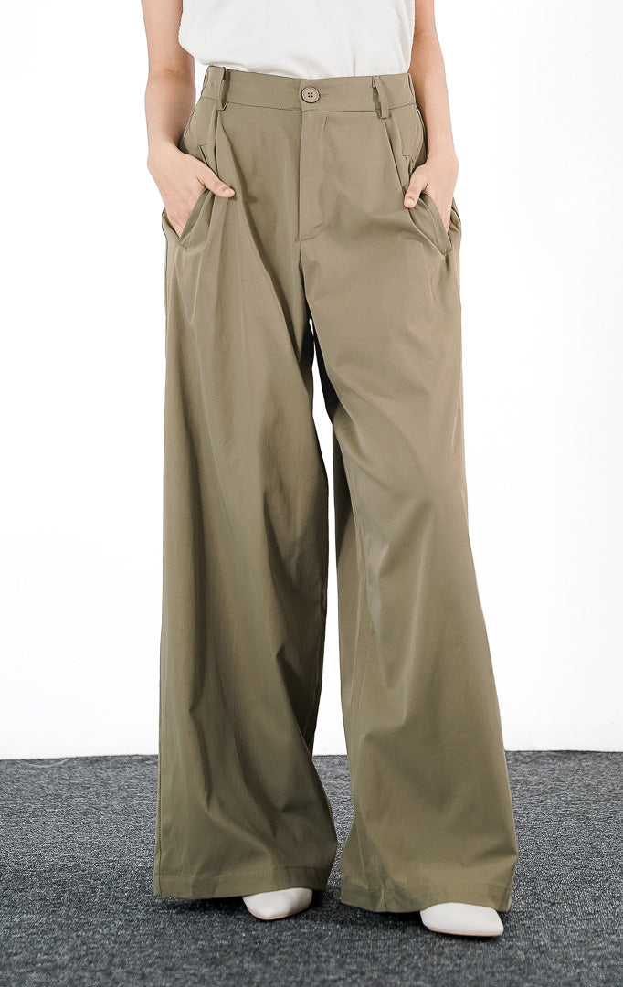 Model mengenakan Nathaniel Pants warna olive, celana panjang bahan dengan potongan lurus (straight leg), saku samping, dan ban pinggang minimalis dengan kancing senada.