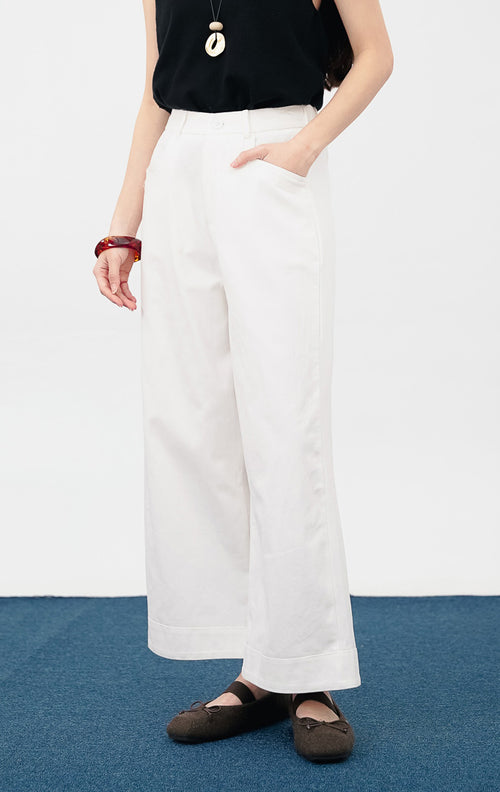 Model mengenakan Oneiros Pants warna white, celana kulot katun dengan potongan kaki lebar yang lurus, saku samping, dan detail kancing depan senada.