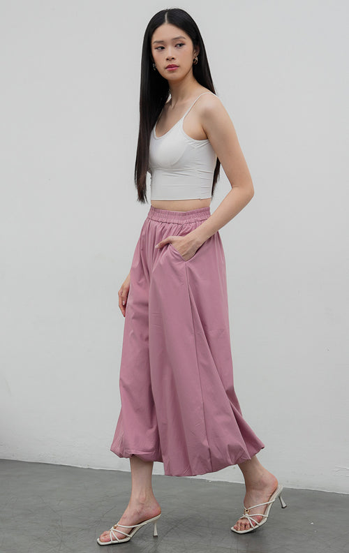 Celana panjang wanita model balon (balloon-leg pants) warna merah muda pudar (dusty pink) Nikolai Pants berbahan campuran katun nilon dengan detail kerut ujung celana (gathered hem) dan pinggang karet.