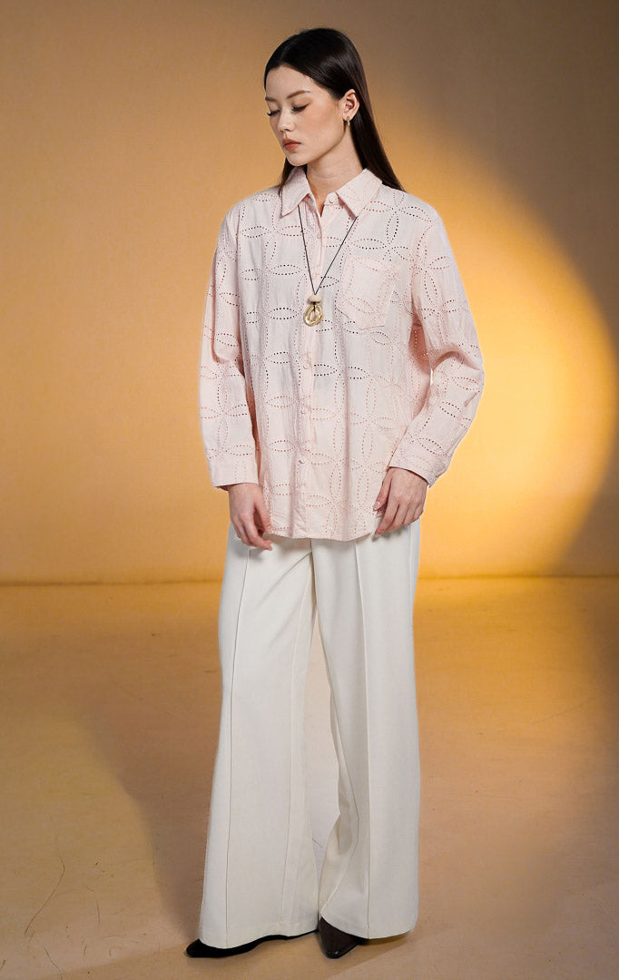Model wanita mengenakan Nome Floral Embroidered Eyelet Shirt warna pink, kemeja lengan panjang kancing depan dengan motif bordir bunga berlubang dan satu saku depan, dipadukan dengan celana panjang putih