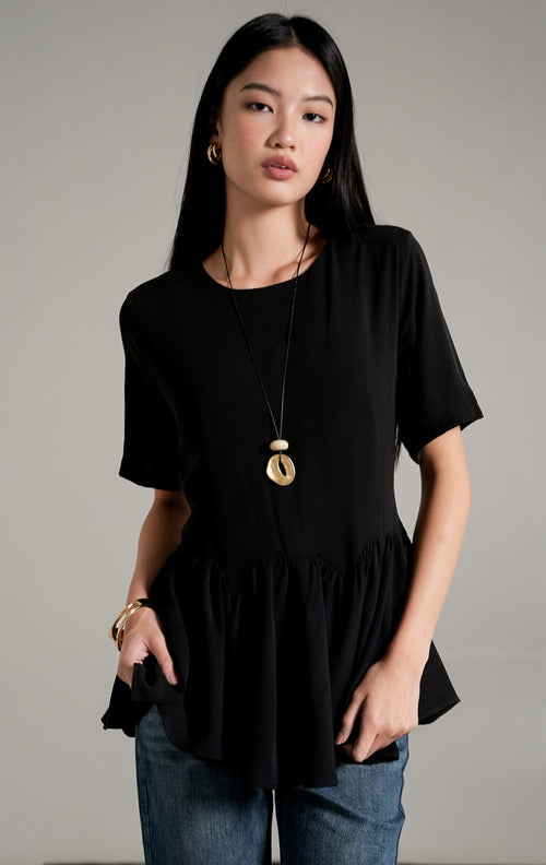 Nyla Top Black, atasan lengan pendek warna hitam dengan detail peplum lebar dan tali serut di pinggang, dipadukan dengan celana jeans flare.