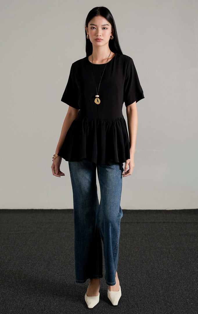Nyla Top Black, atasan lengan pendek warna hitam dengan detail peplum lebar dan tali serut di pinggang, dipadukan dengan celana jeans flare.