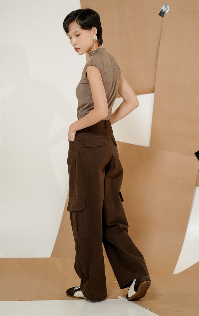 Model berpose menghadap samping belakang mengenakan Oliviana Classic Cargo Pants Dark Brown, produk celana panjang cargo wanita warna cokelat tua dengan detail saku kantong samping.