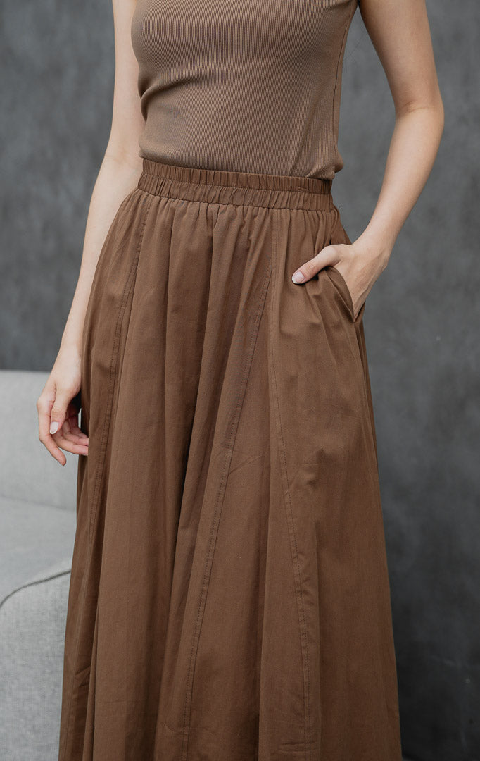 Rok maxi wanita model mekar (flared) warna cokelat tua (dark brown) Ophelia Skirt dengan detail jahitan panel, saku samping, dan pinggang full karet.