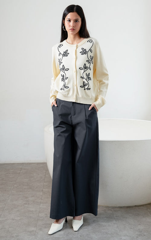 Kardigan rajut wanita lengan panjang warna kuning muda (butter yellow) Oriana Cardigan berbahan soft knit dengan kerah bulat (rounded neckline), bukaan kancing depan, dan bordir motif sulur bunga warna kontras (contrasting floral vine embroidery).