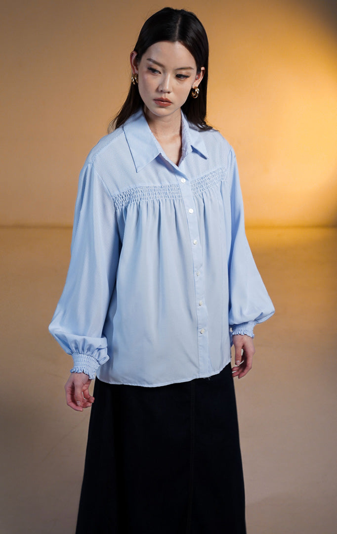 Wanita mengenakan kemeja biru Osiana Smocked Long Sleeve Shirt dengan detail kerutan di dada dan manset lengan panjang
