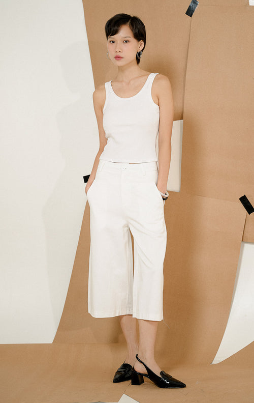 Model berdiri berpose mengenakan Paladia Soft Culottes Pants White, produk celana kulot wanita warna putih dengan potongan wide-leg tanggung dipadukan tank top putih.