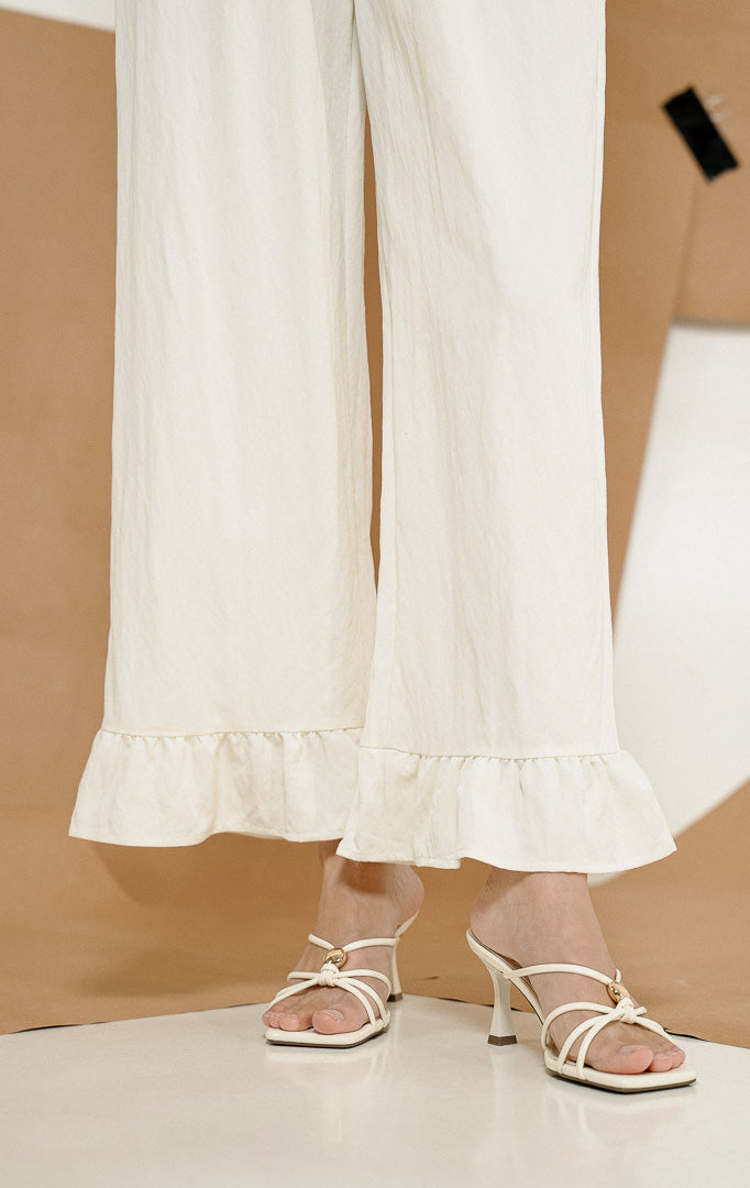 Close-up detail keliman bagian bawah Pericles Pants White, produk celana panjang wanita warna putih dengan aksen ruffle manis di pergelangan kaki.