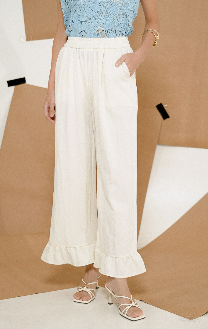 Close-up detail keliman bagian bawah Pericles Pants White, produk celana panjang wanita warna putih dengan aksen ruffle manis di pergelangan kaki.