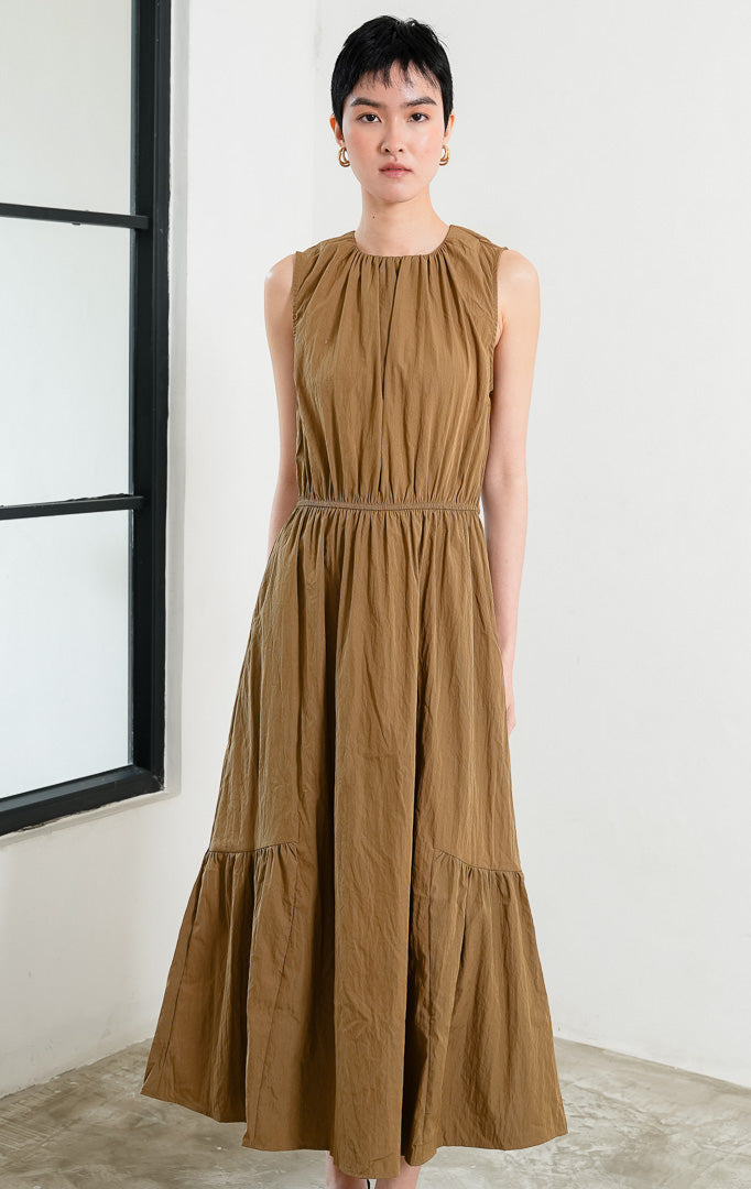 Gaun panjang wanita tanpa lengan (sleeveless maxi dress) warna cokelat muda (light brown) Persephone Dress berbahan crinkle ringan dengan aksen lipit leher (gathered neckline), pinggang karet elastis (elasticated waist), dan rok bertingkat (tiered skirt).