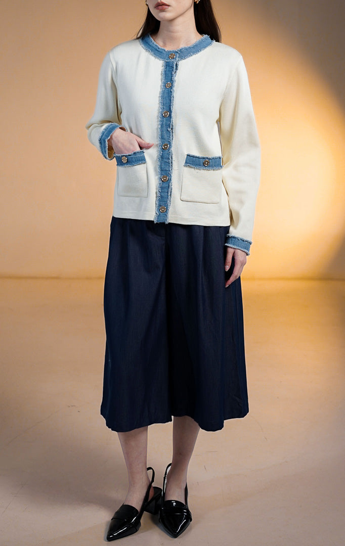 Model wanita mengenakan Peyton Contrast Denim Trim Cardigan, jaket rajut warna putih gading (ivory) dengan list denim biru bertepi serabut (raw edge) pada kerah, saku, dan lengan, serta kancing emas