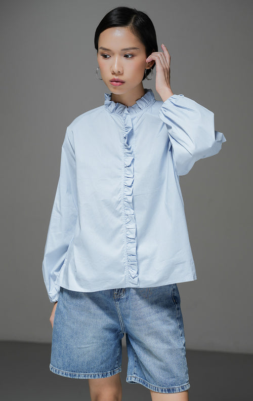 Baju atasan wanita lengan panjang Raffaella Top warna light blue biru muda polos dengan detail kerah ruffle, aksen rumbai lipit di bagian depan, dan pergelangan tangan berkaret.
