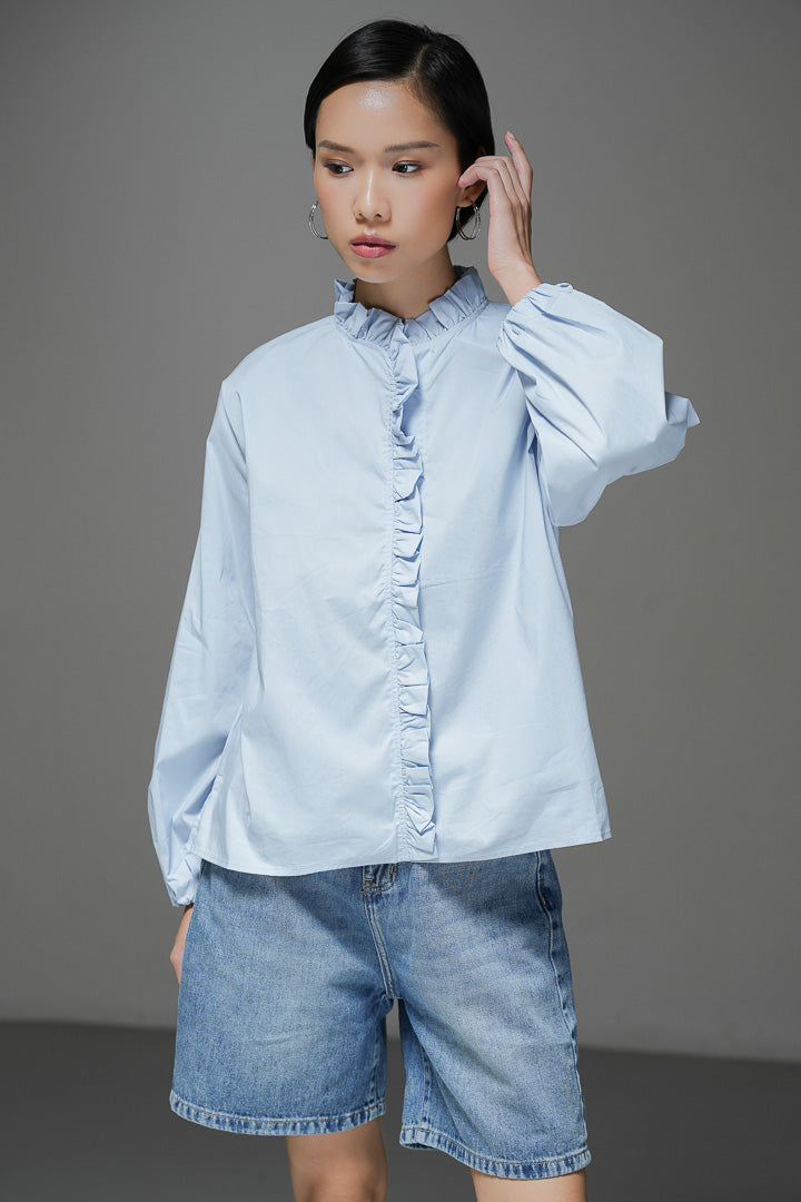 Baju atasan wanita lengan panjang Raffaella Top warna light blue biru muda polos dengan detail kerah ruffle, aksen rumbai lipit di bagian depan, dan pergelangan tangan berkaret.