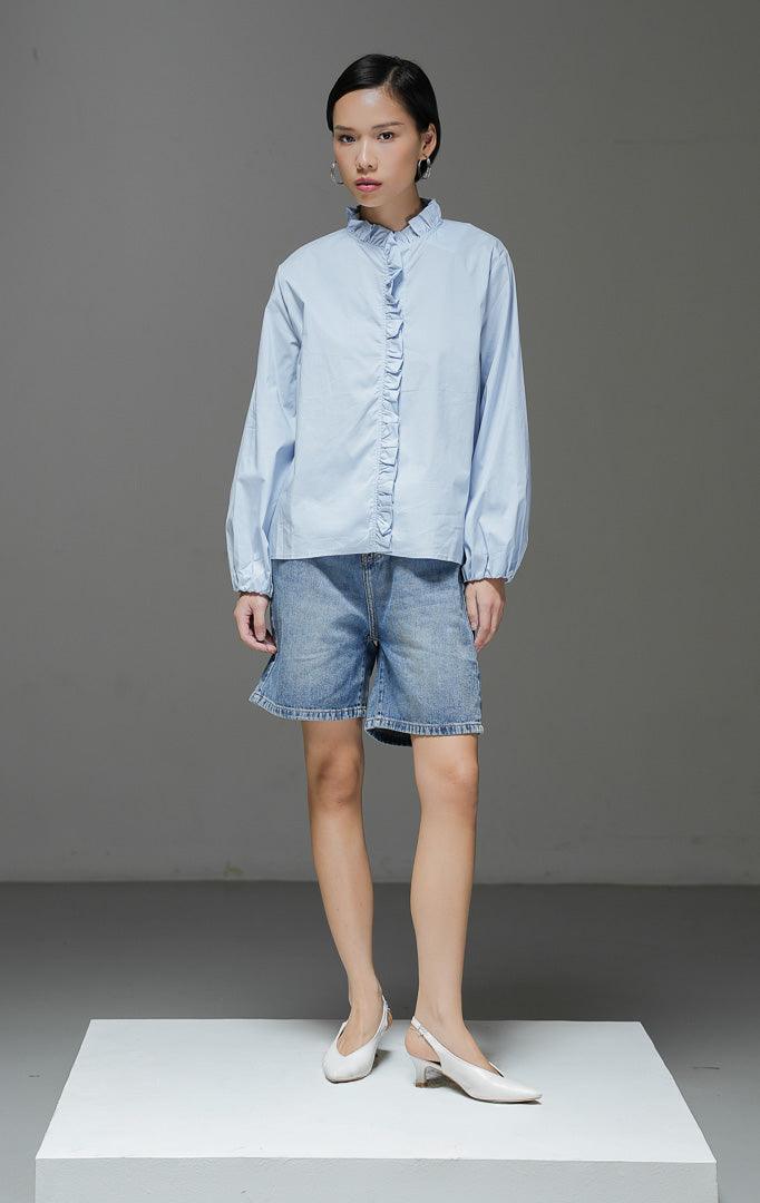 Baju atasan wanita lengan panjang Raffaella Top warna light blue biru muda polos dengan detail kerah ruffle, aksen rumbai lipit di bagian depan, dan pergelangan tangan berkaret.