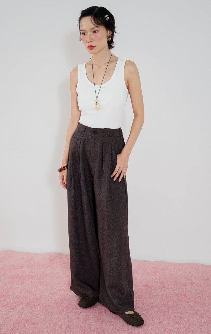 Celana panjang wanita Ramona Pants warna cokelat tua (dark brown) dari This Is April dengan detail lipit depan dan potongan kaki lurus, dipadukan dengan tank top putih.