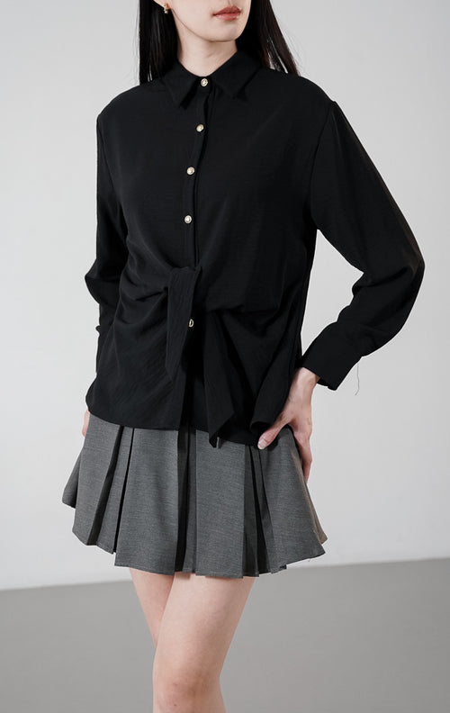 Raphina Top warna hitam, kemeja lengan panjang bertekstur crinkle dengan detail tali pita yang diikat di depan dan kancing emas kontras.1