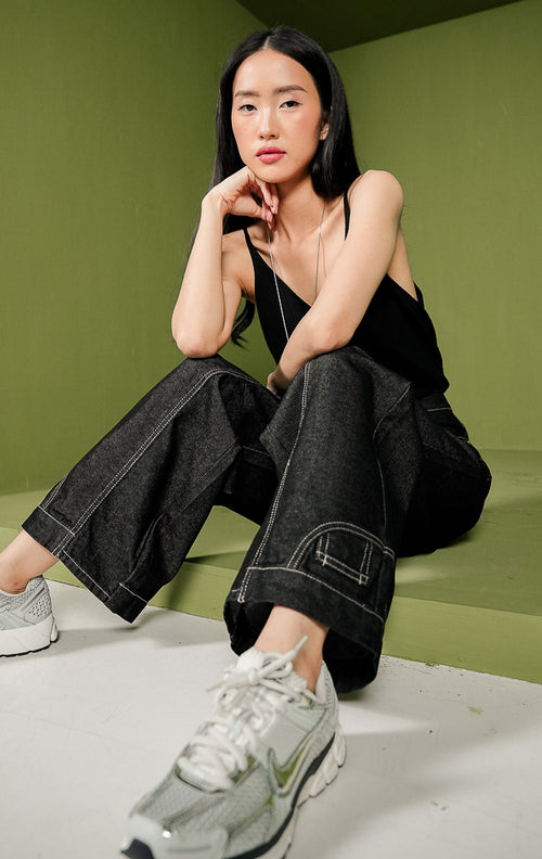 Celana panjang jeans wanita Rencia Pants berpotongan lurus (straight leg) warna indigo gelap, menonjolkan detail jahitan benang putih (contrast stitching) dengan pola garis melengkung di bagian depan paha, dilengkapi kancing metal dan saku klasik.