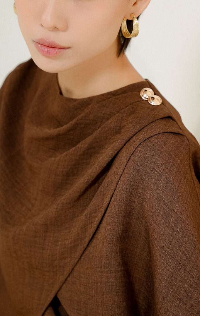 Close-up detail kerah dan bahu Rhayn Wrap Blouse Top Dark Brown, menampilkan tekstur kain cokelat tua dengan desain silang wrap dan dua kancing emas dekoratif.