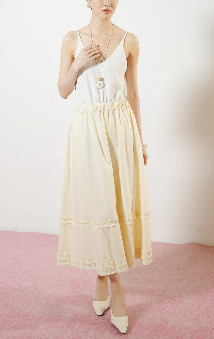 Model wanita mengenakan Arabella Skirt warna ivory, rok midi panjang wanita berwarna putih tulang dengan pinggang karet dan detail aksen kerut ruffle horizontal.