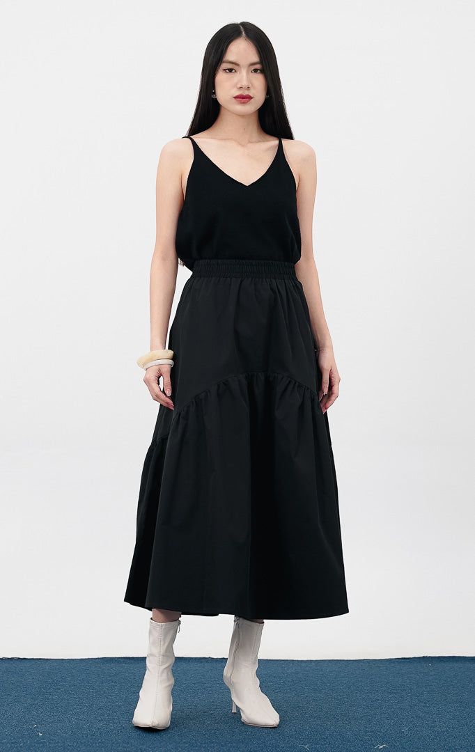 Model mengenakan Rosalia Skirt warna black, rok panjang dengan detail pinggang elastis dan potongan bertingkat (tiered) yang melebar di bagian bawah.