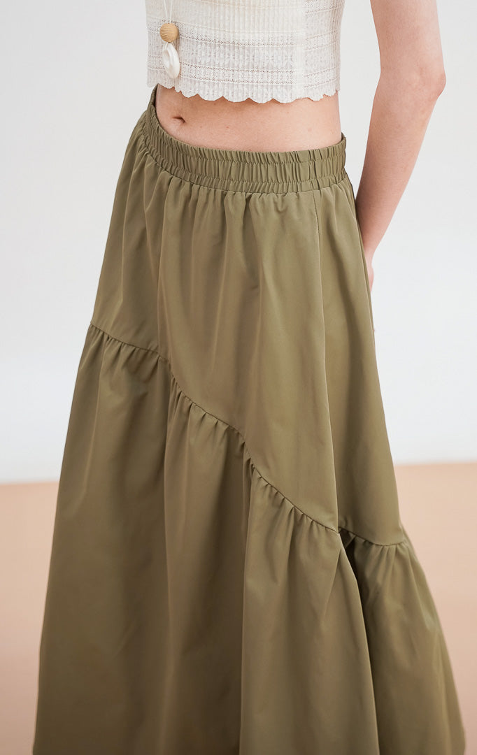 Model mengenakan Rosalia Skirt warna dark green, rok panjang bertingkat (tiered) dengan detail pinggang elastis, dipadukan dengan crop top broken white.