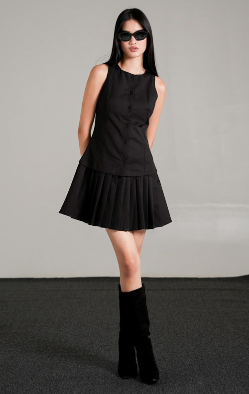 Rosemary Dress Black, gaun mini tanpa lengan warna hitam dengan kancing depan dan rok lipit pendek, dipadukan dengan kacamata hitam dan sepatu boots tinggi.