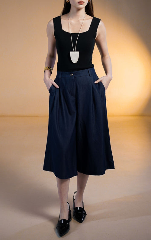 Model wanita memakai Ruben Pants Dark Denim, celana kulot bermuda lebar warna biru tua dengan saku samping, dipadukan dengan tank top hitam dan kalung putih