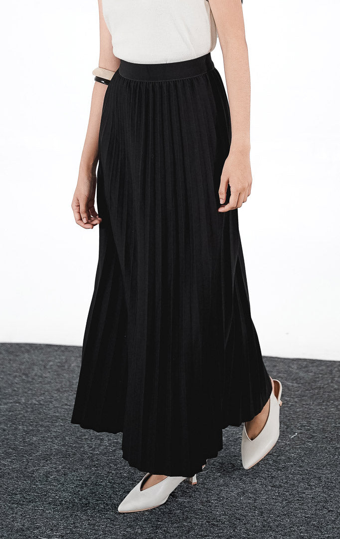 Ryka Skirt warna hitam, rok midi plisket (pleated) siluet A-line yang rapi dengan ban pinggang elastis, dipadukan dengan atasan tanpa lengan putih.1