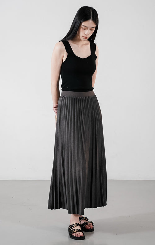 Ryka Skirt warna dark grey, rok midi plisket (pleated) siluet A-line yang rapi dengan ban pinggang elastis, dipadukan dengan sandal hitam.