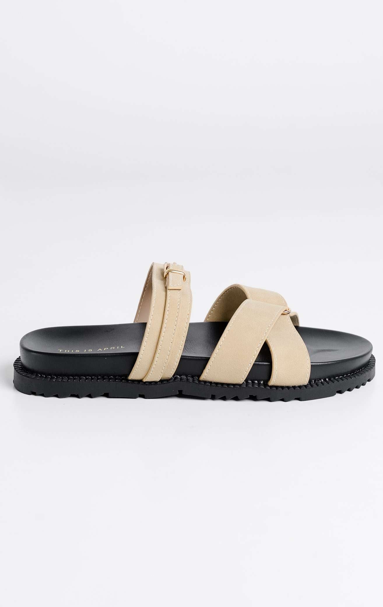 Tampilan depan sepasang Violet Sandals warna beige, sandal flat teplek wanita tali menyilang bahan suede krem dengan gesper emas dan sol tebal gerigi hitam dari This Is April.