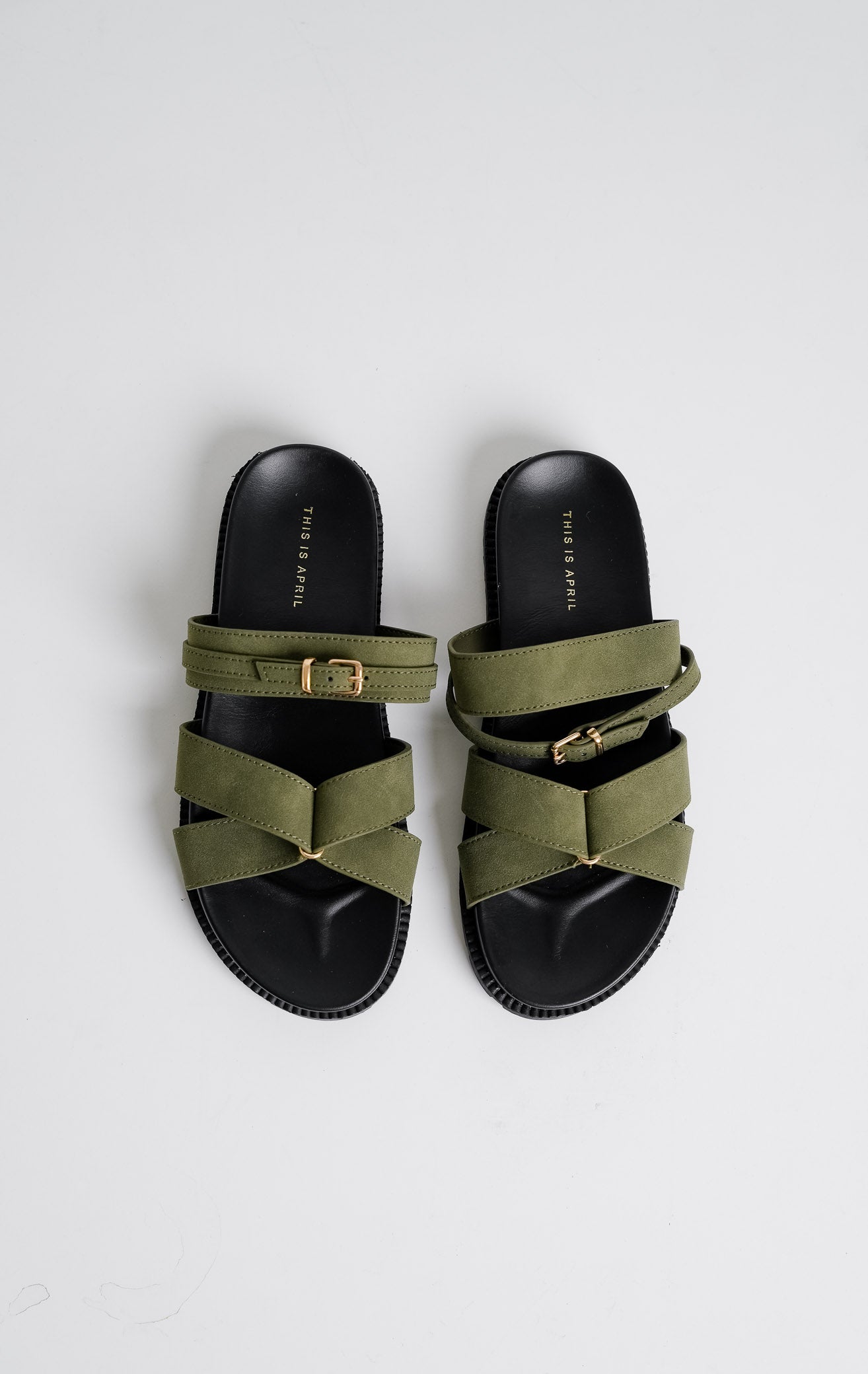 Tampilan flat lay sepasang Violet Sandals warna olive, sandal flat teplek wanita tali menyilang bahan suede hijau zaitun dengan gesper emas dan sol tebal gerigi hitam dari This Is April.