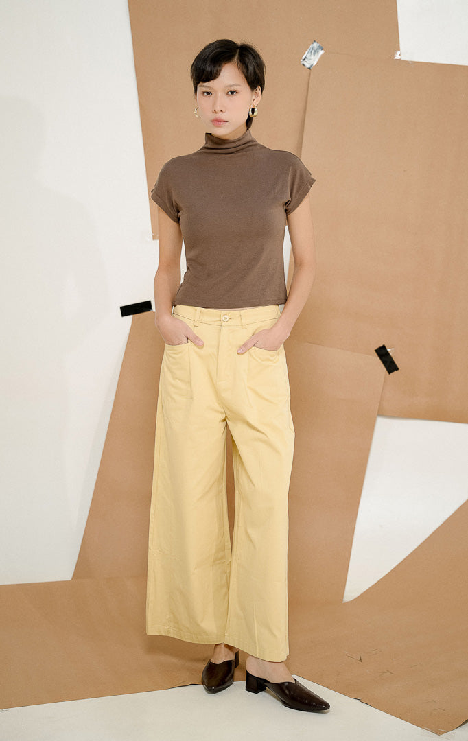 Model berdiri dengan tangan di saku mengenakan Sapphire Straight Leg Pants Yellow, produk celana panjang wanita potongan lurus warna kuning lembut dengan detail kancing depan.