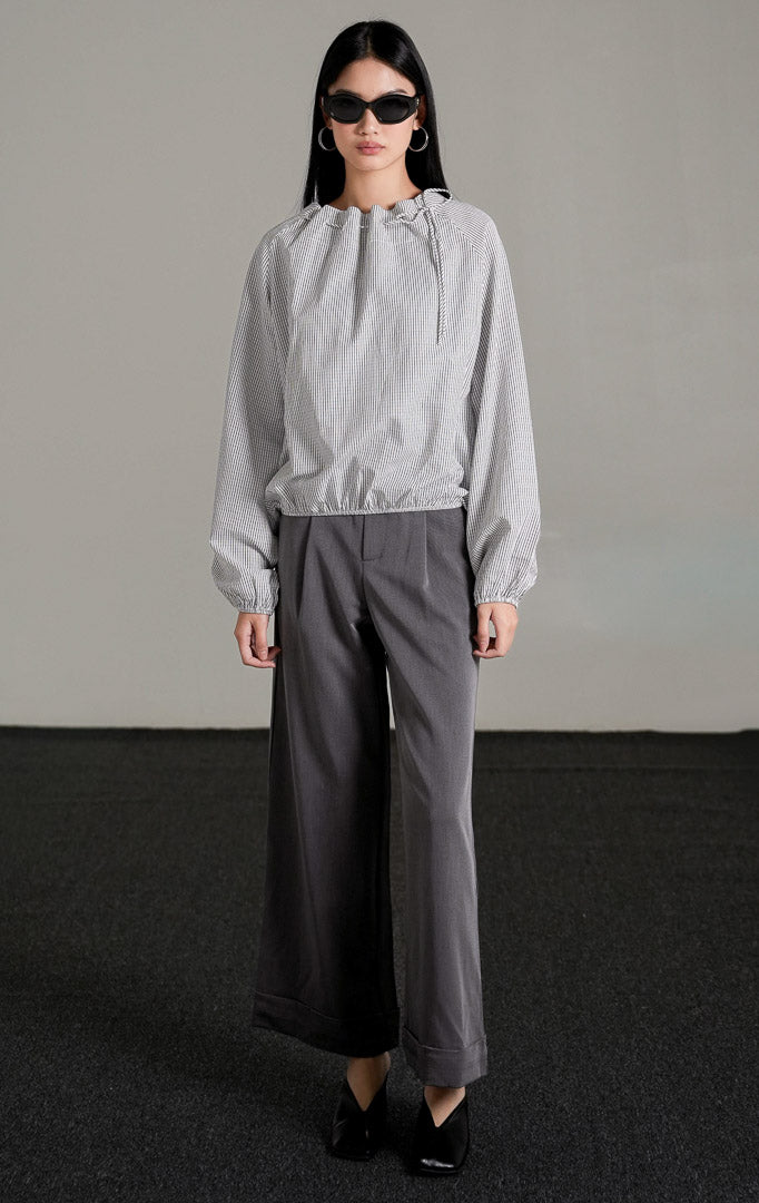 Seraph Top White, atasan katun putih motif kotak grid halus dengan leher serut (drawstring), dipadukan dengan celana kulot abu-abu dan kacamata hitam.