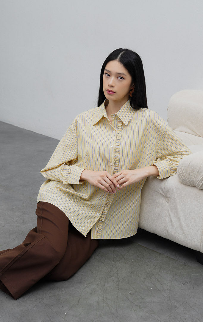 Kemeja katun wanita lengan panjang warna kuning (yellow) Sevran Top berkerah dengan motif garis vertikal (vertical stripes), detail rumbai (ruffle trim), dan bukaan kancing depan.