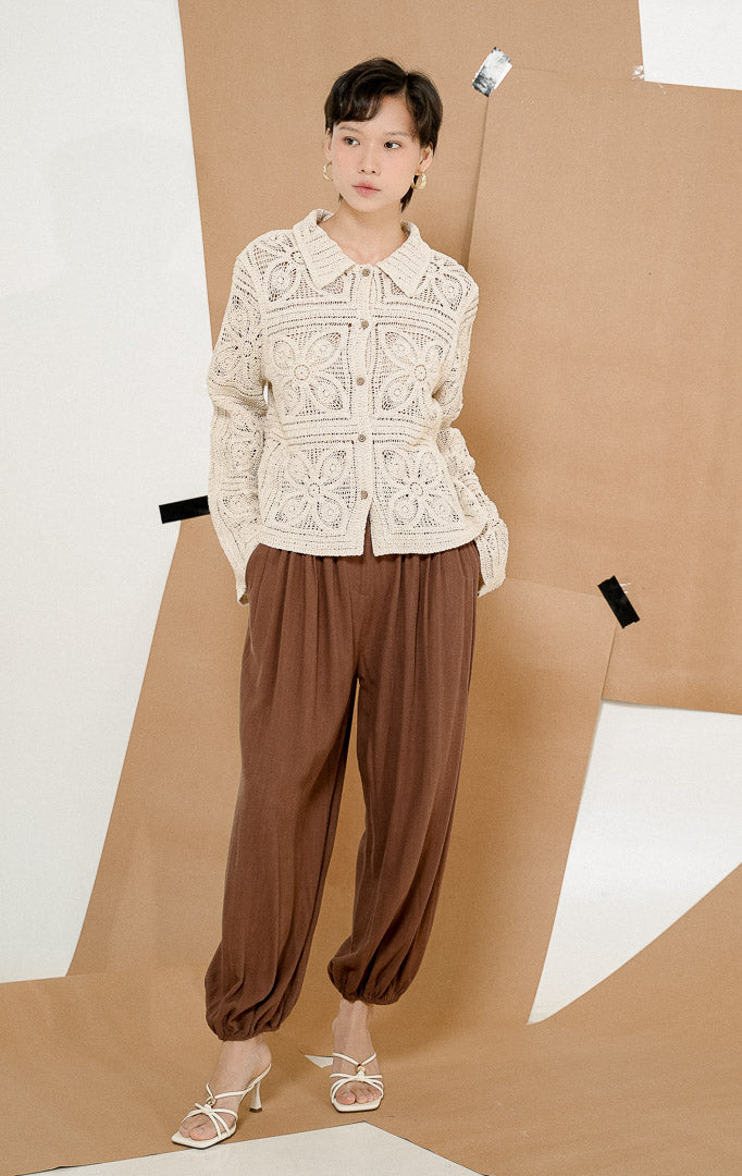 Model berpose jongkok mengenakan Sevyn Granny Square Crochet Cardigan Ivory, luaran cardigan rajut wanita lengan panjang warna krem dengan motif rajutan transparan.