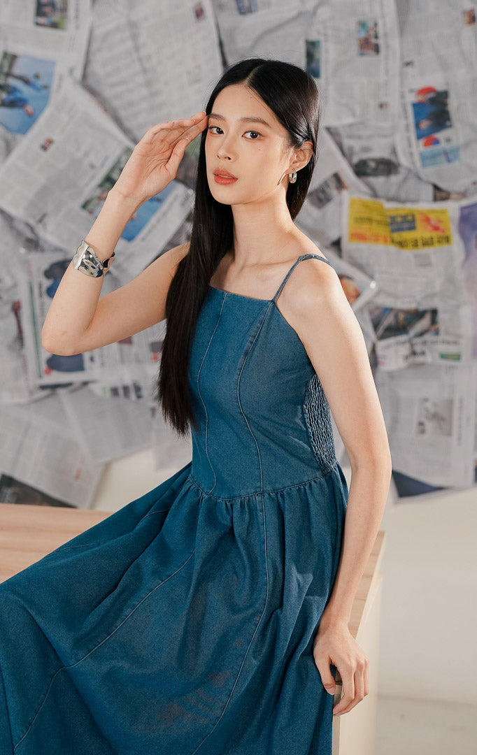 Model mengenakan Shanon Dress Denim, sebuah maxi dress wanita bahan denim biru yang kokoh, model tanpa lengan (sleeveless) dengan potongan panjang yang santai dan elegan.