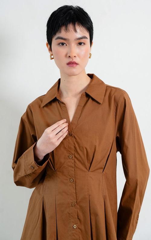 Kemeja wanita lengan panjang warna cokelat (brown) Shea Top dengan kerah kemeja (pointed collar), leher V (V-neckline), bukaan kancing depan, dan detail lipit di pinggang (pleated waist).