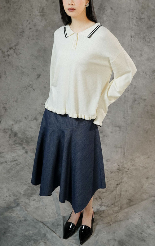 Sweater rajut lengan panjang wanita Sinclair warna ivory dengan kerah polo klasik, aksen ruffle, serta detail list garis putih di ujung lengan dan hem bawah.