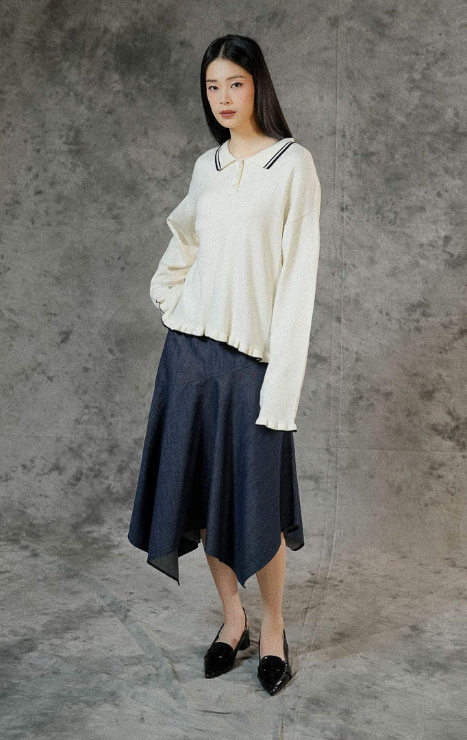 Sweater rajut lengan panjang wanita Sinclair warna ivory dengan kerah polo klasik, aksen ruffle, serta detail list garis putih di ujung lengan dan hem bawah.