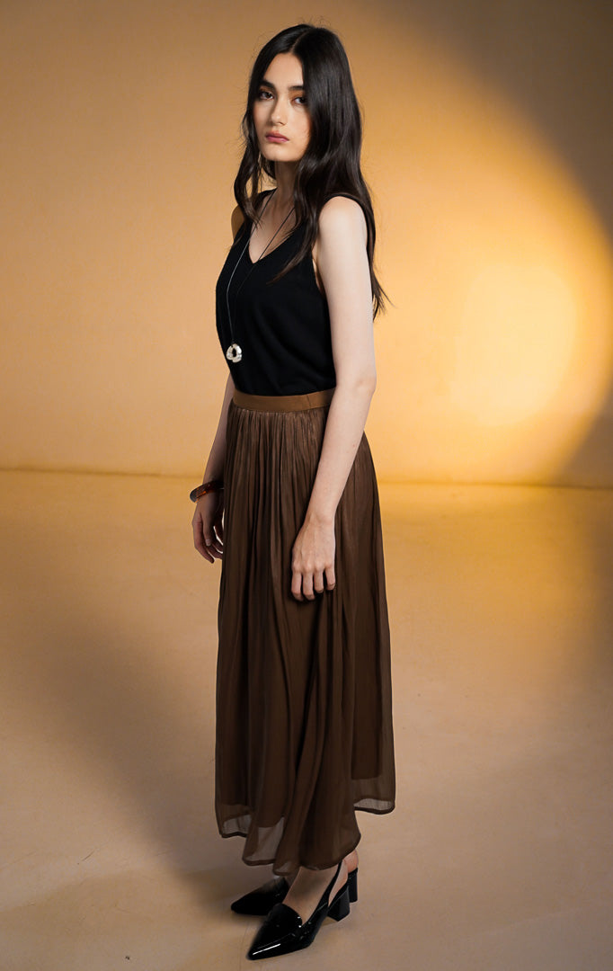Model wanita memakai Sinclair Skirt Dark Brown, rok midi bahan chiffon tekstur crinkle metallic warna coklat tua dengan pinggang karet elastis.