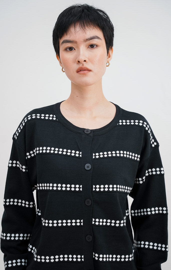 Model mengenakan Soleil Cardigan warna black, kardigan rajut lengan panjang dengan motif garis horizontal titik-titik putih dan kancing bulat hitam di bagian depan.