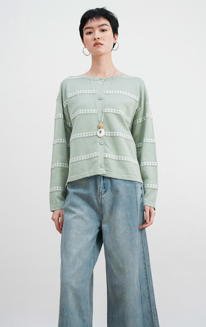 Model mengenakan Soleil Cardigan warna sage, kardigan rajut lengan panjang dengan motif garis horizontal titik-titik putih dan kancing depan senada