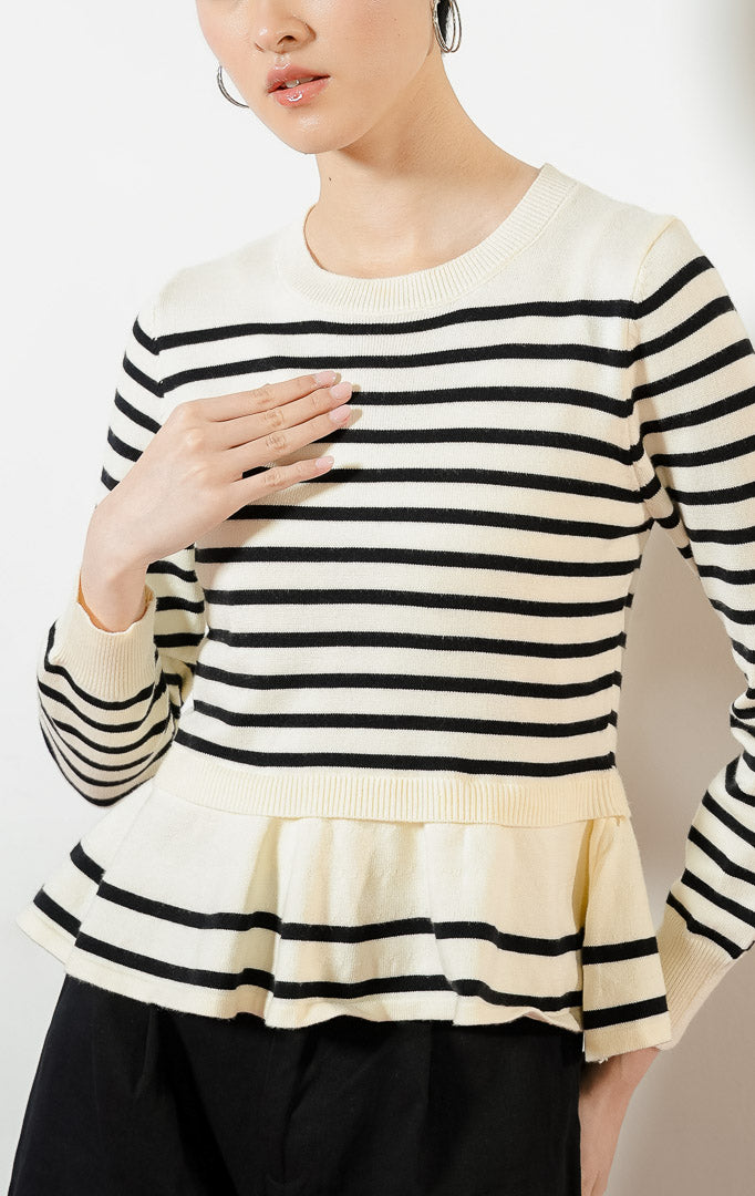 Model wanita mengenakan Season Striped Ruffle Hem Knit Sweater warna ivory, atasan sweater baju rajut wanita lengan panjang motif garis salur putih hitam dengan detail kelim peplum rumbai yang feminin.