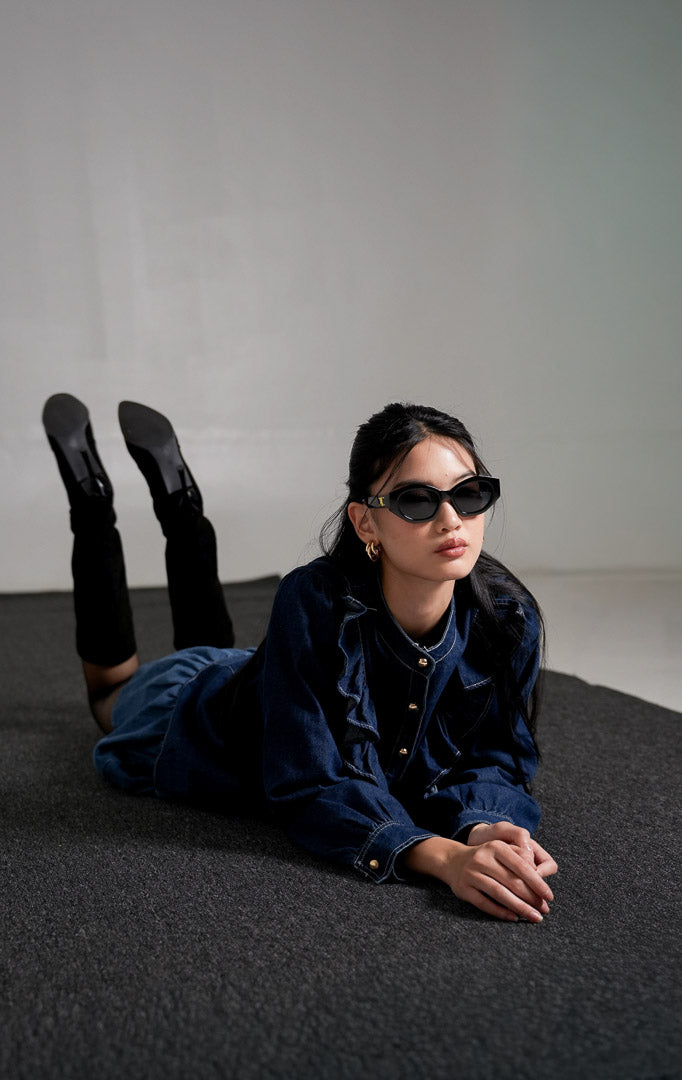 Sylvain Top Dark Denim, kemeja denim biru tua dengan detail ruffle asimetris di bagian dada dan kancing emas, dipadukan dengan rok mini denim senada