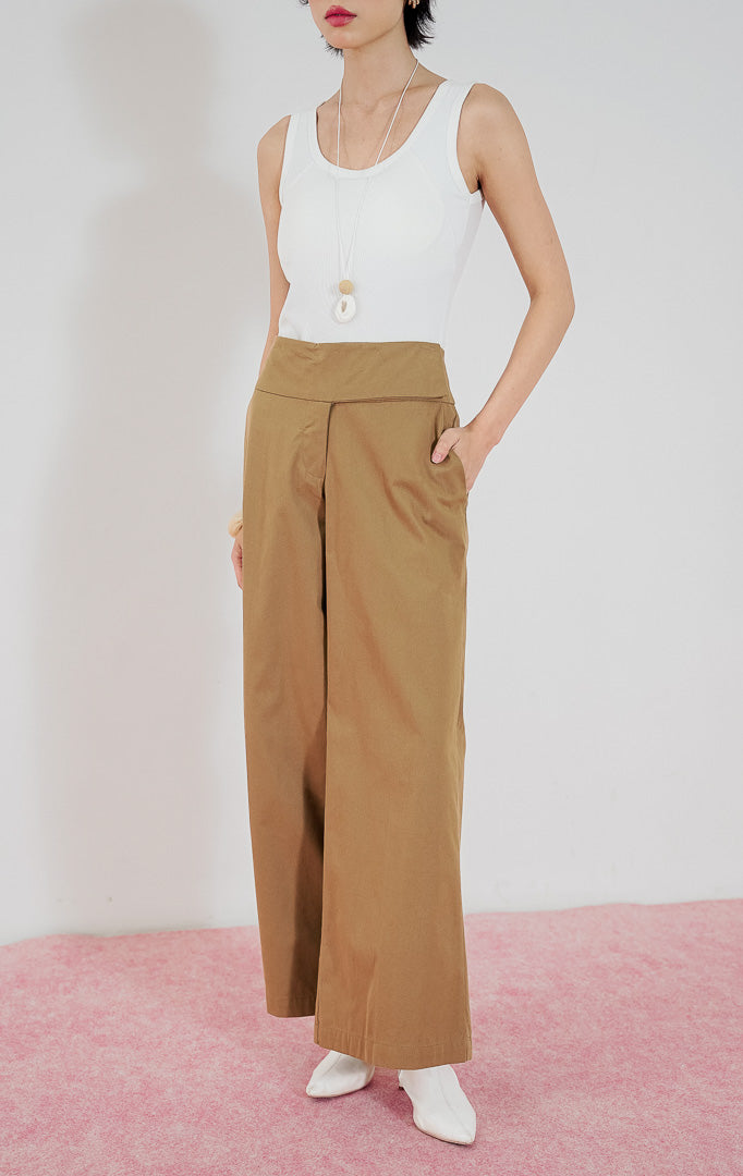 Celana panjang wanita Taffyra Pants warna cokelat (brown) dari This Is April dengan potongan high-waisted dan kaki lebar (wide leg), dipadukan dengan tank top putih.