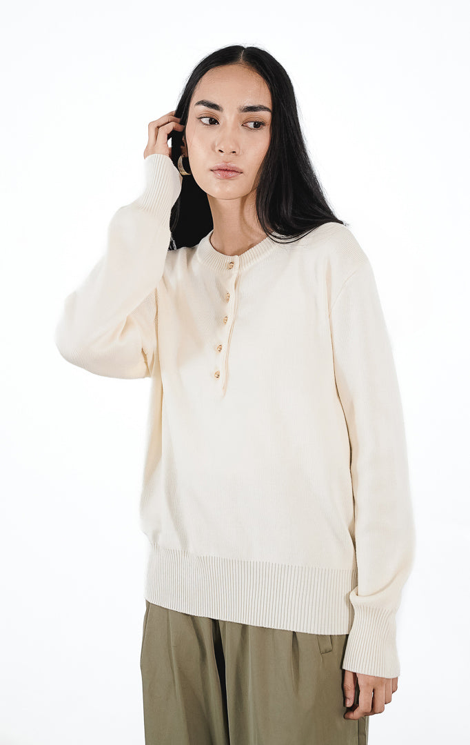 Model mengenakan Talia Cardigan warna ivory, atasan rajut lengan panjang dengan detail kancing emas kecil di bagian depan atas dan siluet rapi.