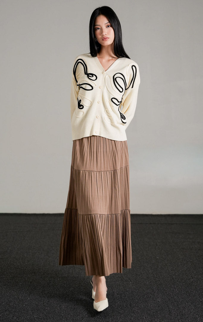 Thea Patterned Knit Cardigan, kardigan rajut warna broken white dengan motif garis melengkung hitam, dipadukan dengan rok panjang cokelat.