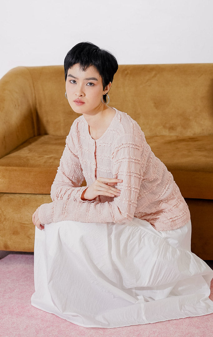 Outer crop wanita lengan panjang Anandra Top dari This Is April berwarna dusty pink dengan detail tekstur ruffle renda horizontal berlapis, kancing depan mutiara, dan material sheer menerawang, digantung di rak pakaian
