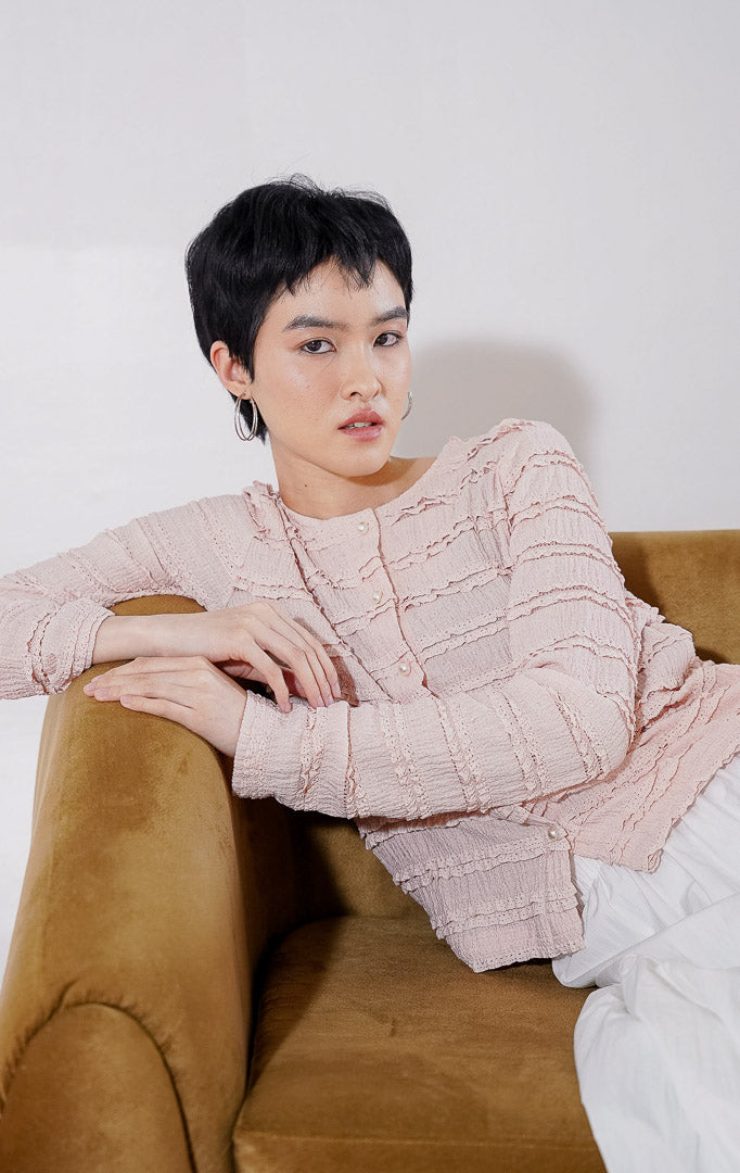 Outer crop wanita lengan panjang Anandra Top dari This Is April berwarna dusty pink dengan detail tekstur ruffle renda horizontal berlapis, kancing depan mutiara, dan material sheer menerawang, digantung di rak pakaian